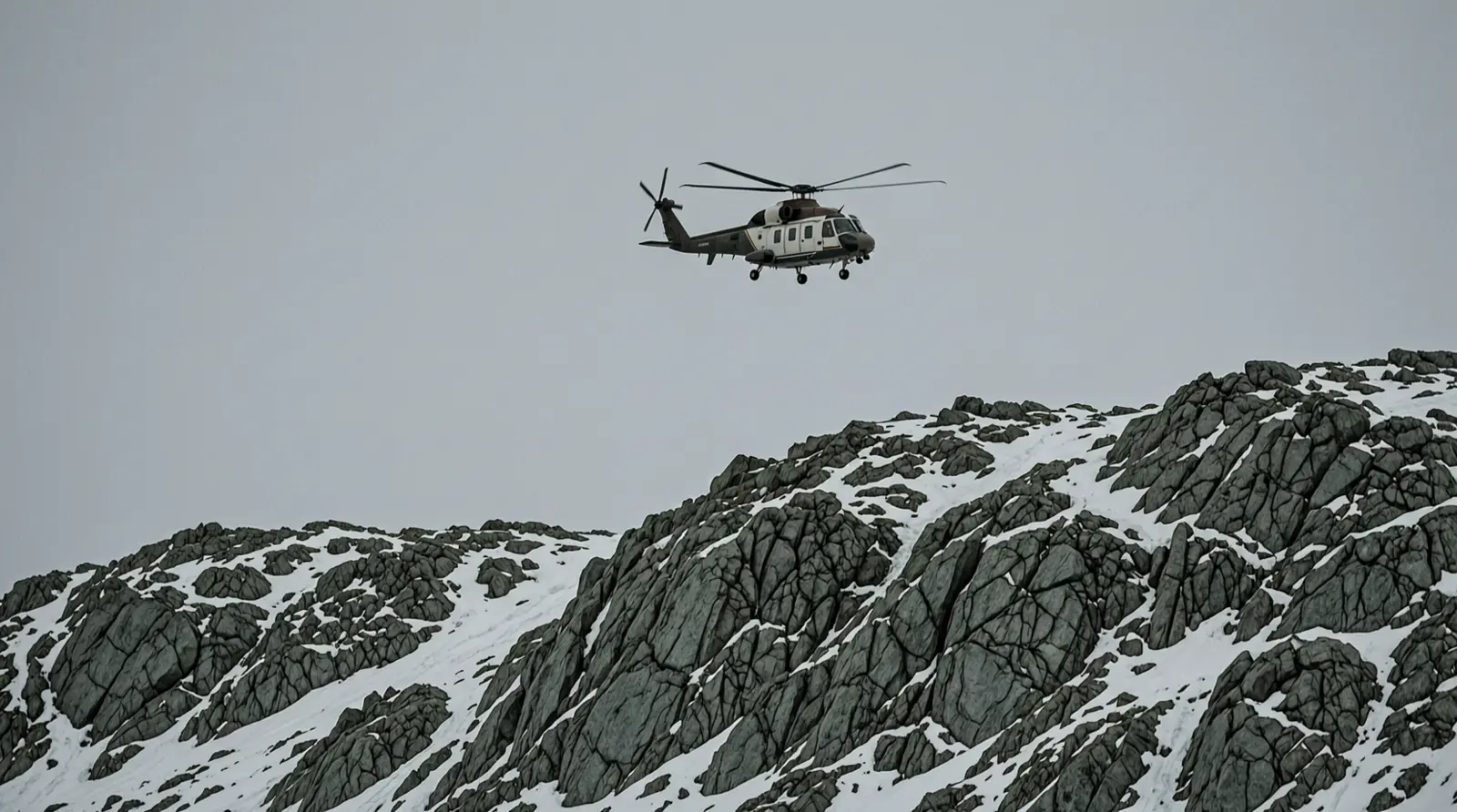 A helicopter flying above a rocky Arctic ridge, seen from far enough away that no markings are visible.