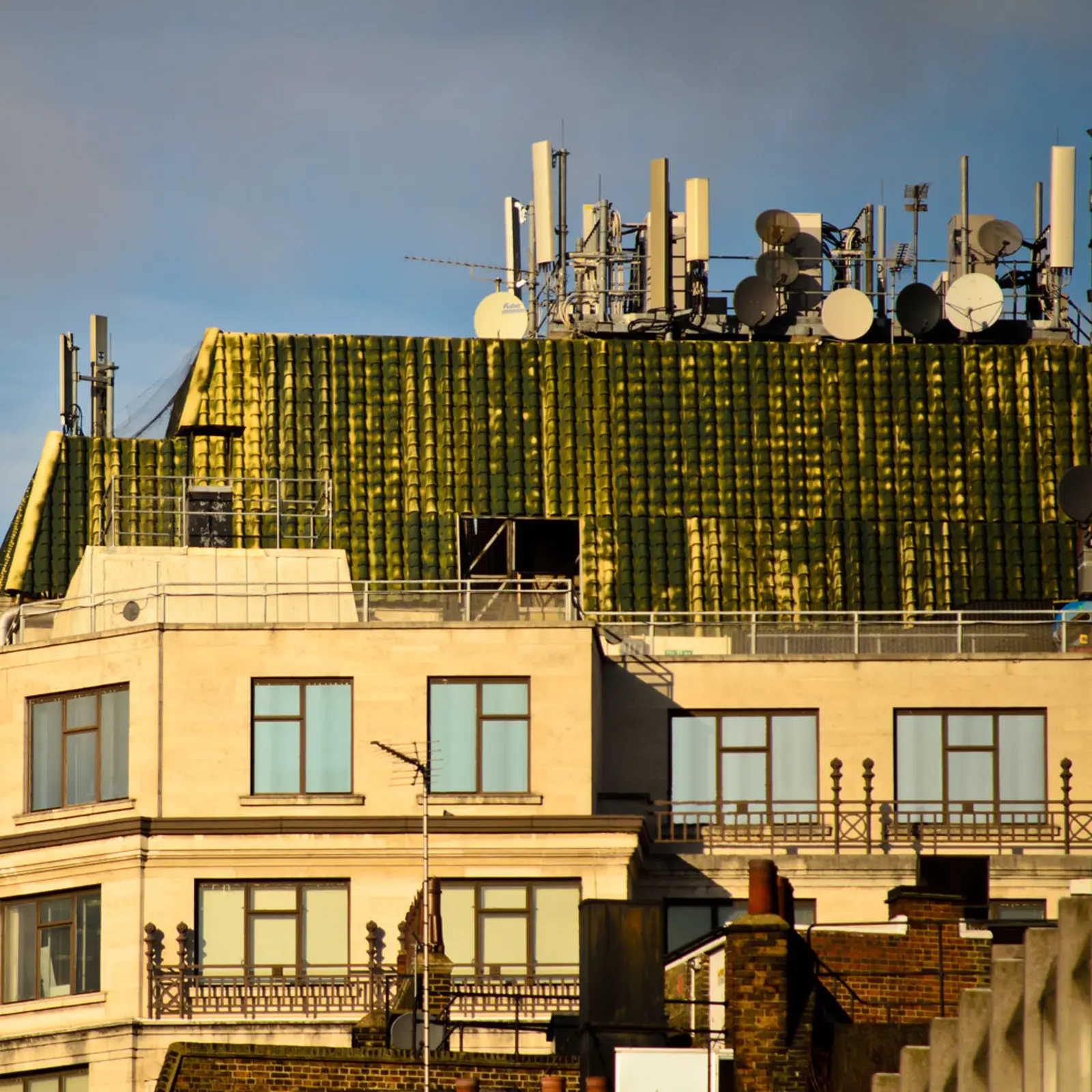 A building with a green tiled roof is topped with a dense array of antennas and satellite dishes. The photographer titled it “Comms”.