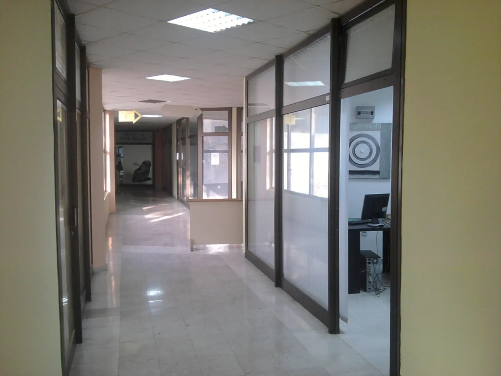 A brightly lit office hallway with glass partitions, frosted lower panels, and a computer monitor visible through an open doorway on the right. The photographer titled it “Start-up office's hall”.