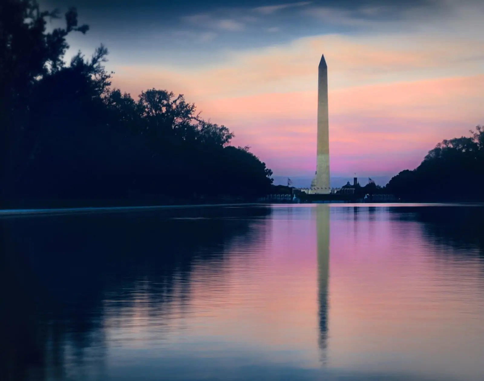 The Washington Monument stands against a pink and blue twilight sky, its reflection cast on a calm body of water in the foreground. The photographer titled it “Dusk on Washington monument”.