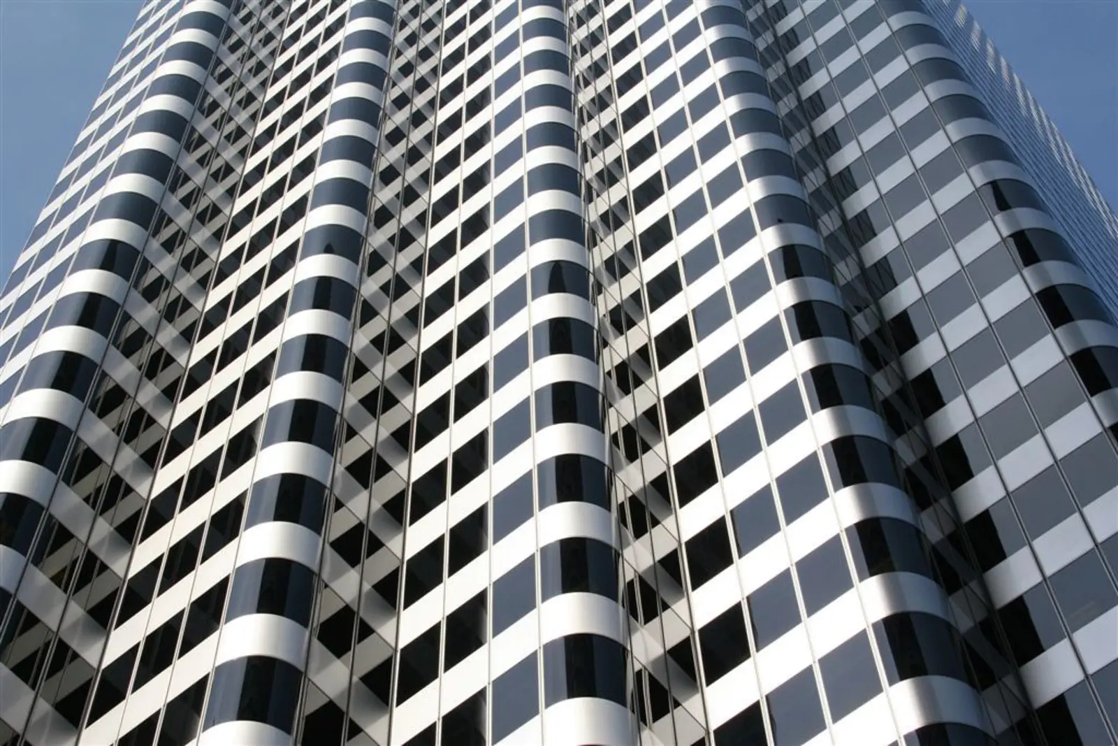 A low-angle, close-up view of a modern skyscraper featuring curved white bands and dark, reflective windows against a clear blue sky. The photographer titled it “Building”.