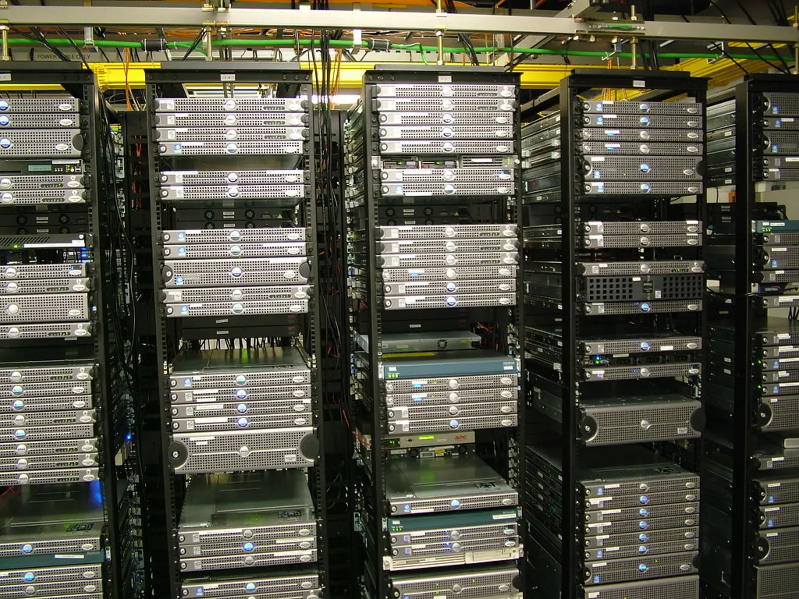 Multiple black server racks filled with silver and black computer hardware units stand side-by-side in a facility.