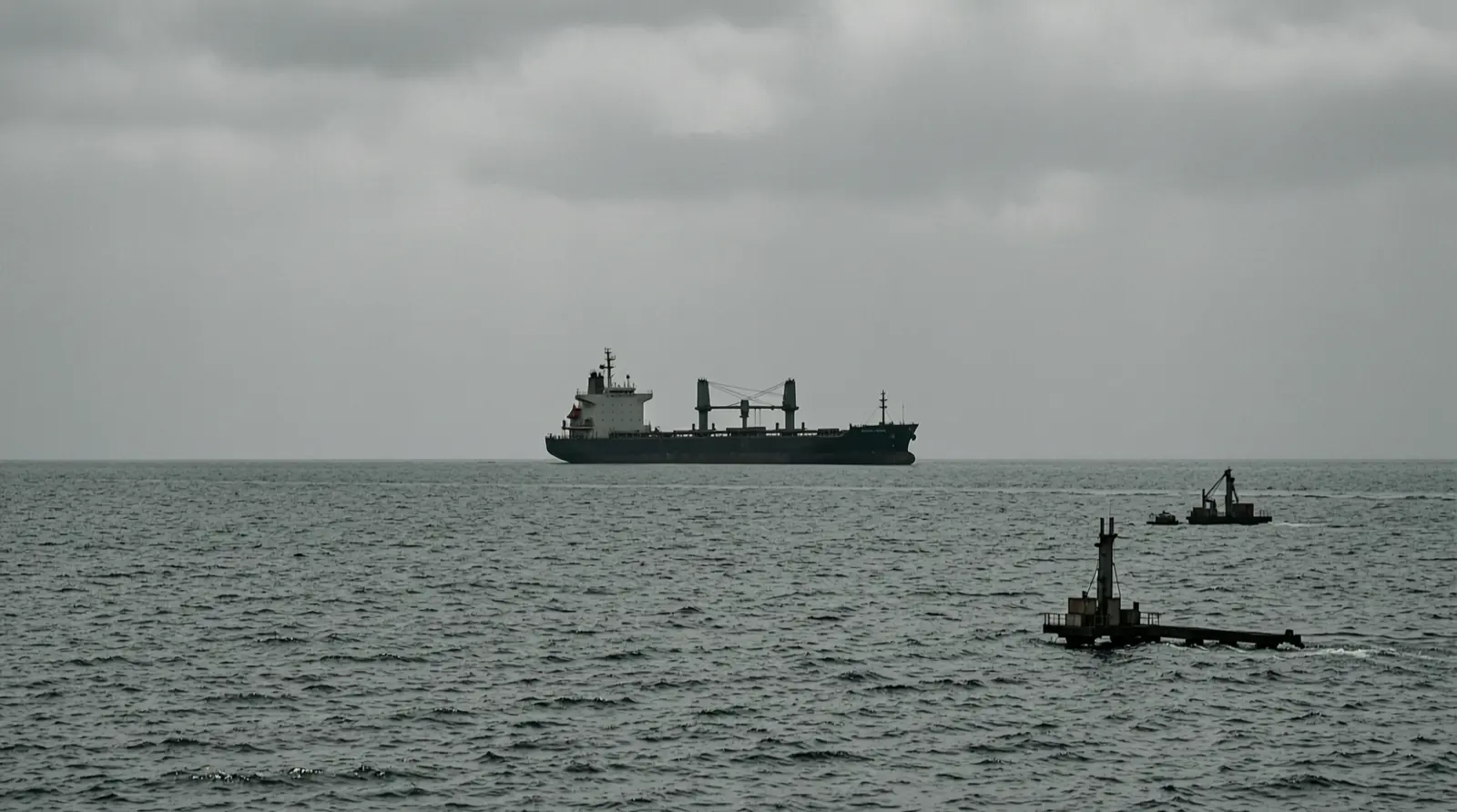 A distant tanker low on the horizon in open water, under a cloudy sky.