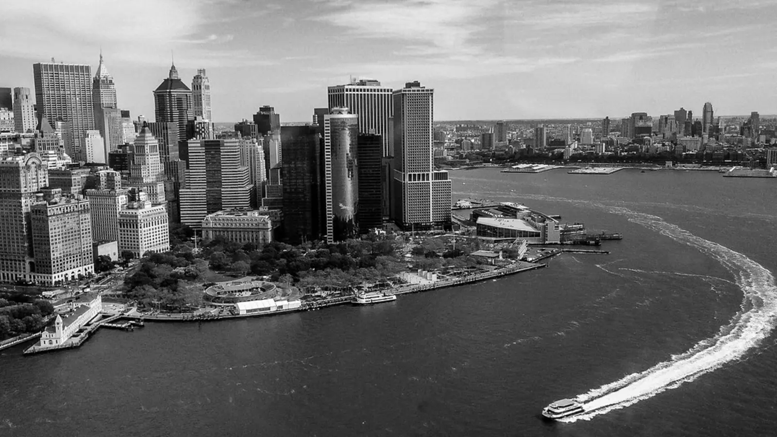 A black-and-white aerial view shows a dense city skyline along the waterfront, with a boat leaving a long wake across the dark water. The photographer titled it “The Edge of Manhattan”.