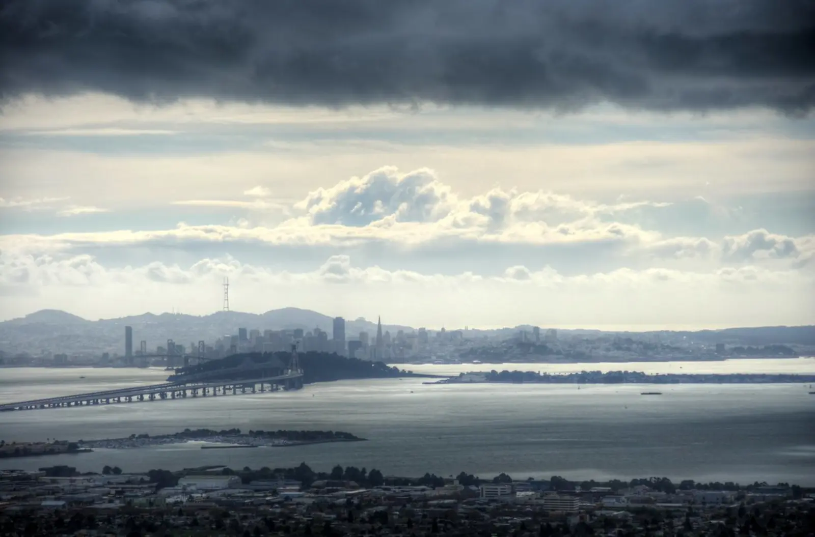 A city skyline is visible across a body of water, situated beneath a sky filled with heavy, dark clouds. The photographer titled it “Storm Clouds over San Francisco”.