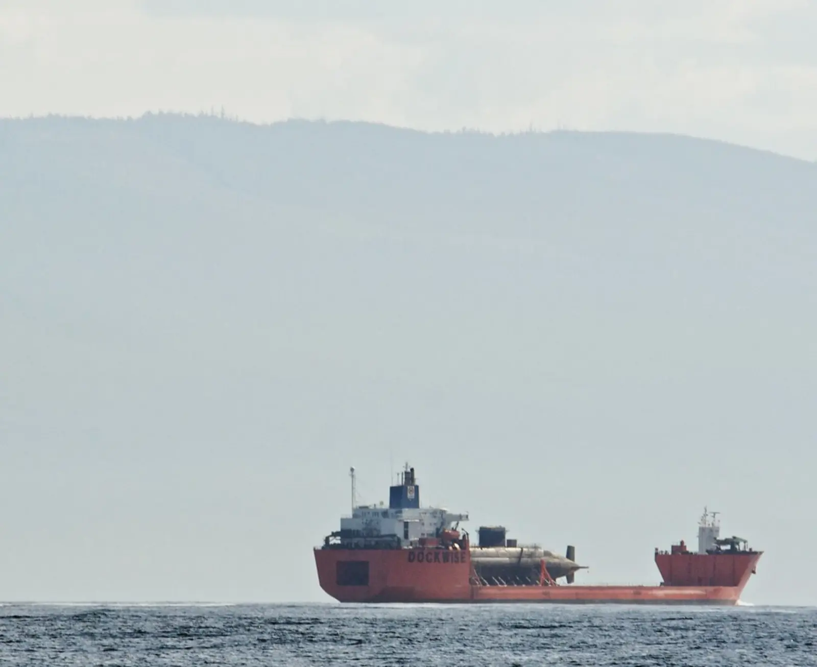 A red cargo ship carrying a large cylindrical load navigates the water against a backdrop of hazy hills. The photographer titled it “High and Dry”.