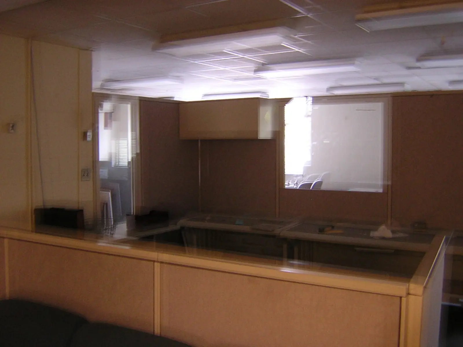 An interior view of an empty office space features beige partition walls, a low counter, and a window looking into an adjacent room. The photographer titled it “old sidelines office — news/opinions”.