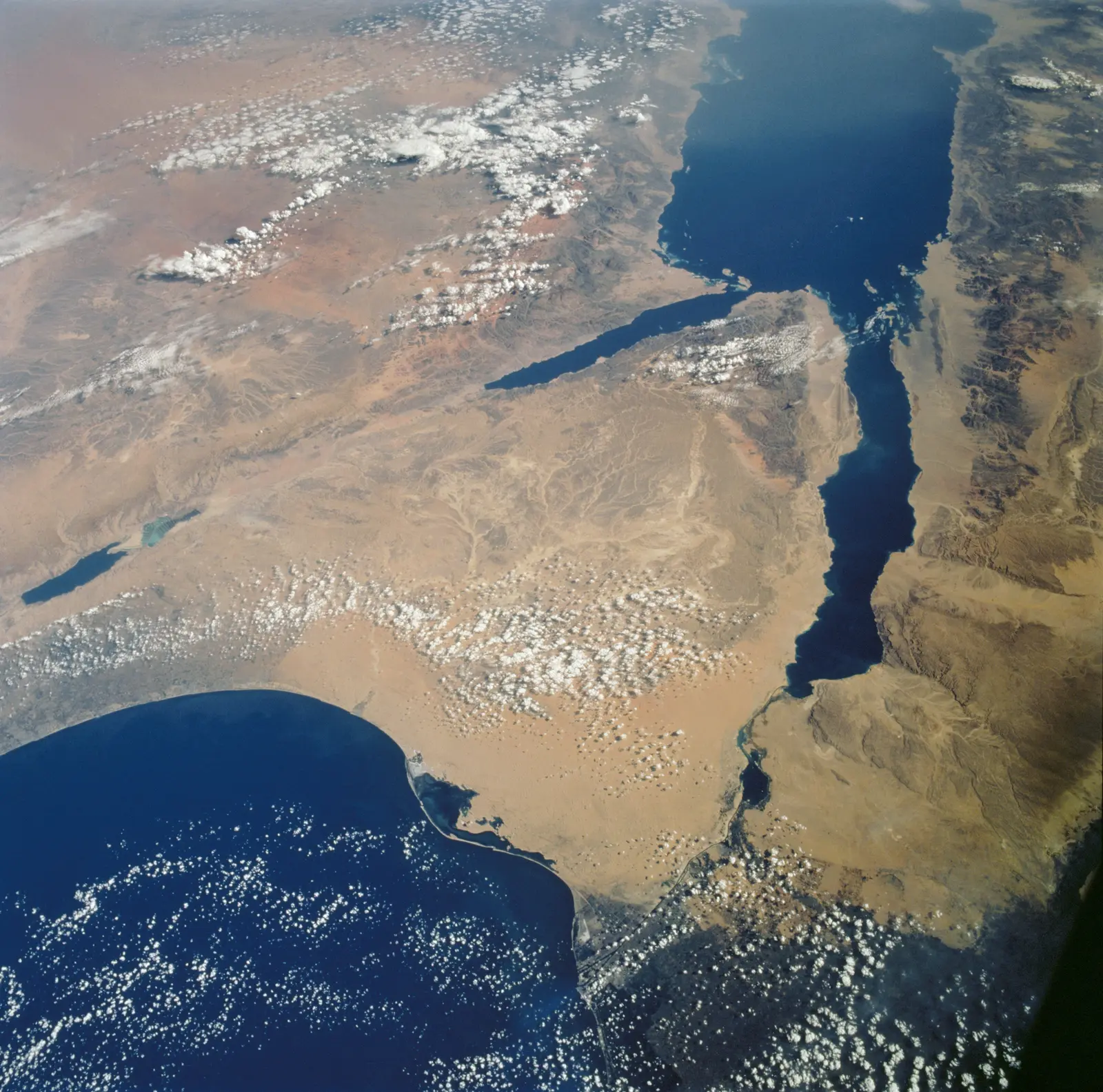 A space photograph shows the arid, tan landscape of the Sinai peninsula bordered by deep blue bodies of water. The photographer titled it “Sinai peninsula taken by the STS-112 crew”.