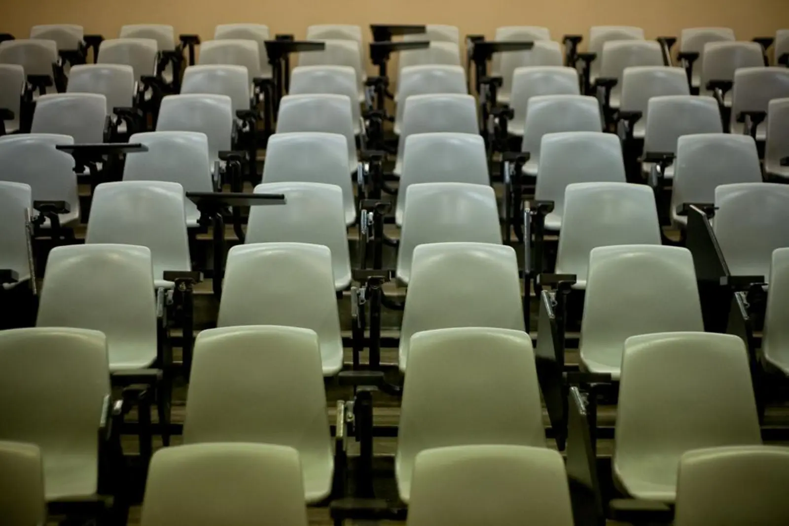 Rows of empty white auditorium seats with attached writing tablets fill a tiered lecture hall.