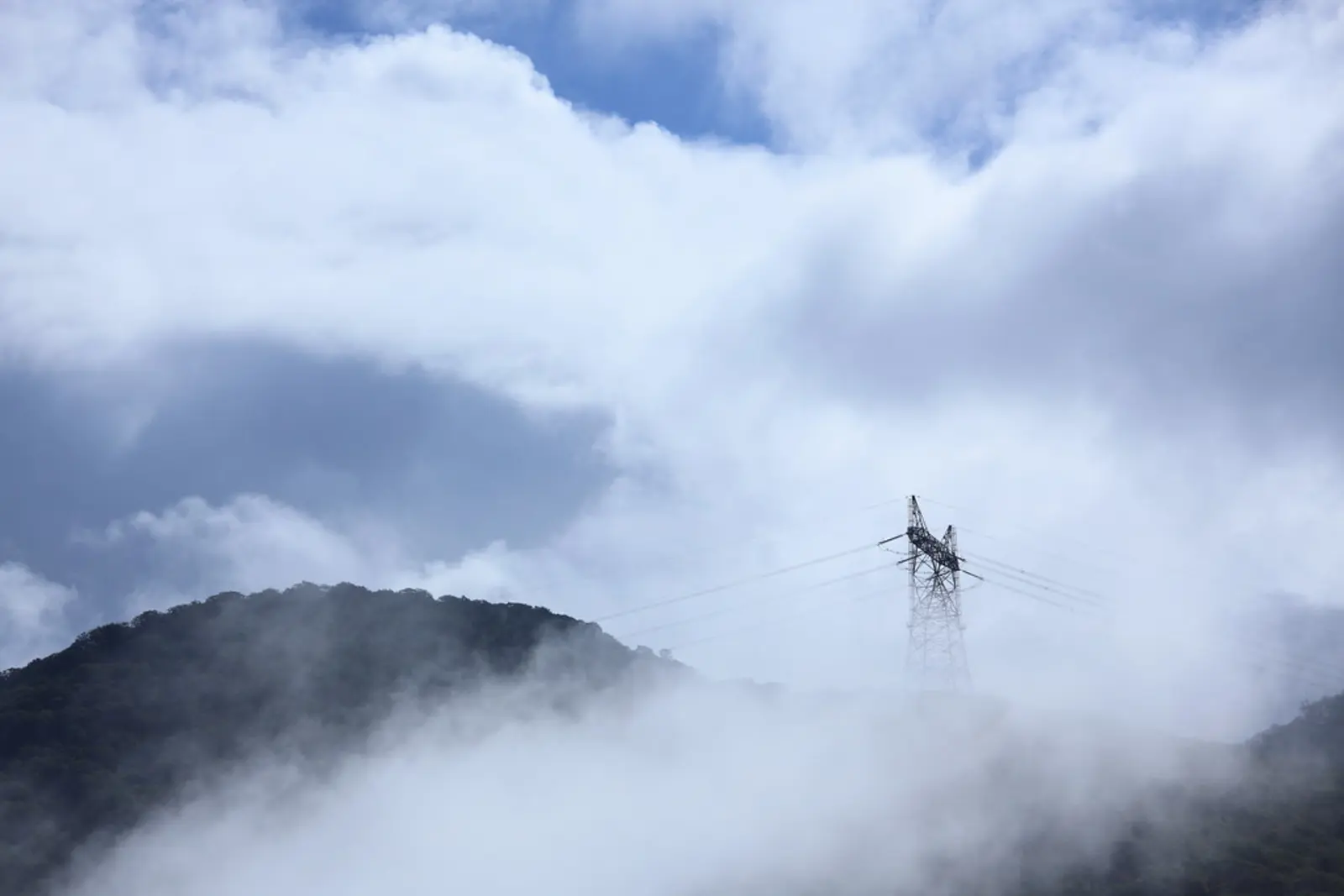 A steel transmission tower stands amidst thick fog and low clouds over a forested mountain ridge. The photographer titled it “Transmission Tower / 鉄塔(てっとう)”.