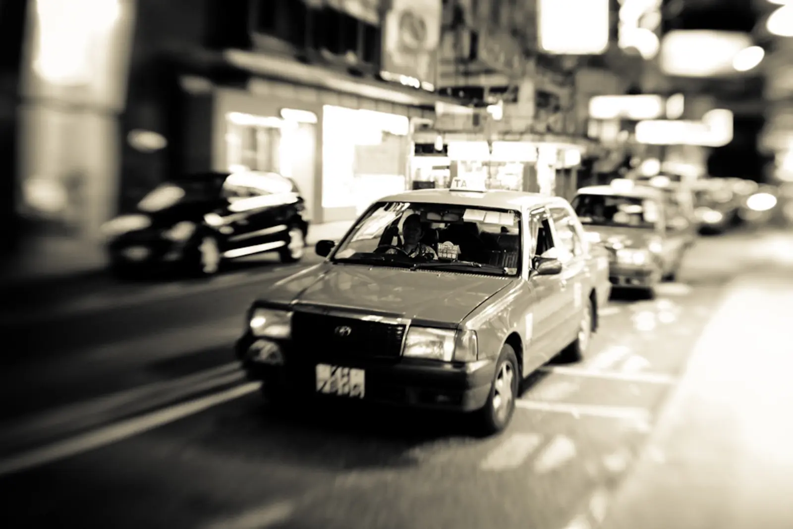 A silver taxi drives down a city street at night, with other cars and illuminated storefronts in the blurred background. The photographer titled it “3AM Hong Kong taxi - Tsim Sha Tsui”.