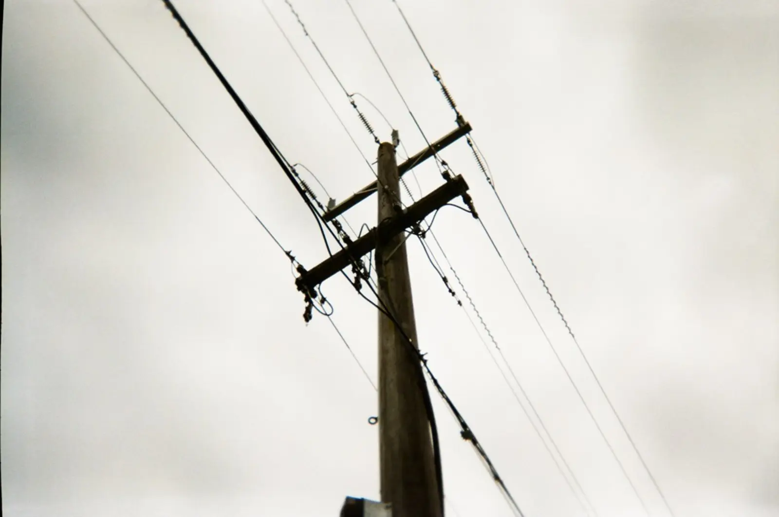 A wooden utility pole with crossarms, insulators, and multiple power lines stands against a blank, overcast sky. The photographer titled it “Power lines pole and overcast sky”.